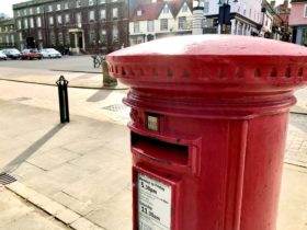 Picture of a bright red post box with large grand buildings behind
