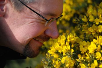David Falk (Festival Director) smiling and sniffing bright yellow gorse flowers